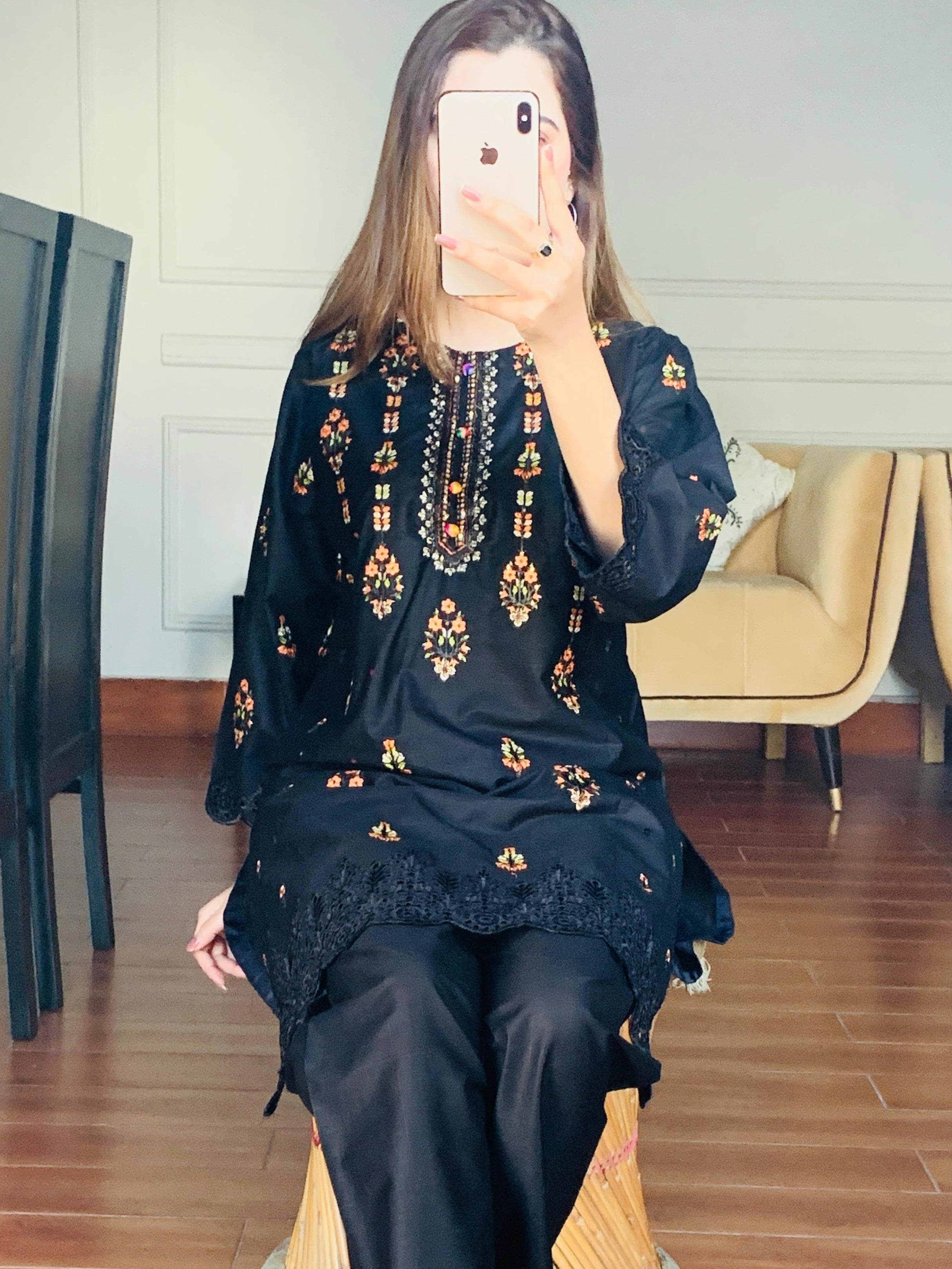 Person wearing a dark blue embroidered outfit sitting on a stool in a room with wooden flooring.
